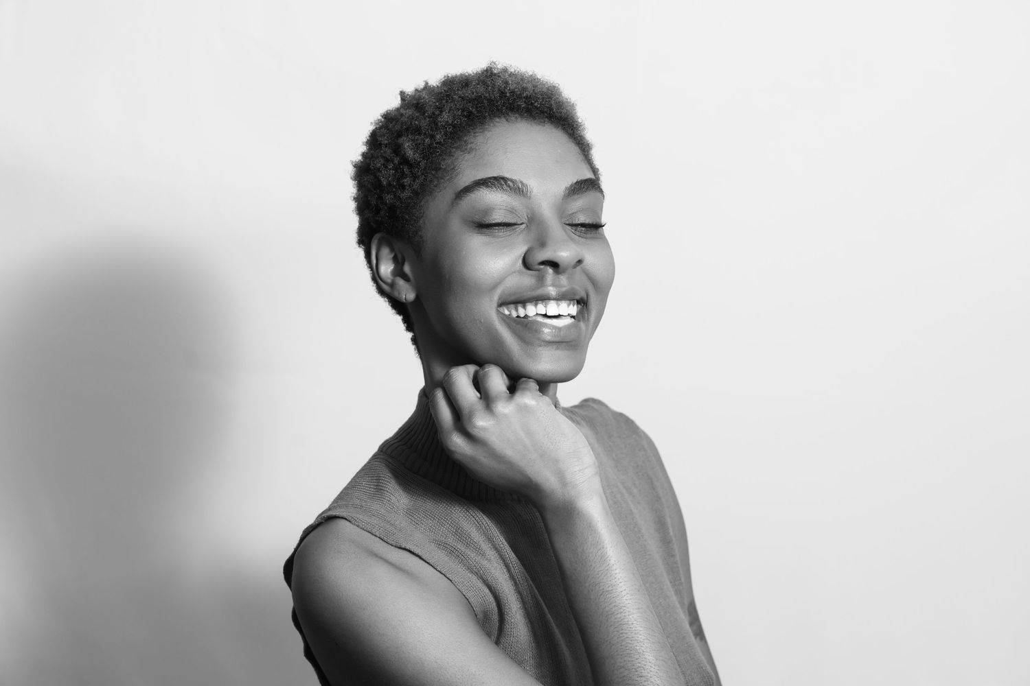 Black and white portrait of a smiling young woman with short hair, eyes closed, hand near chin.