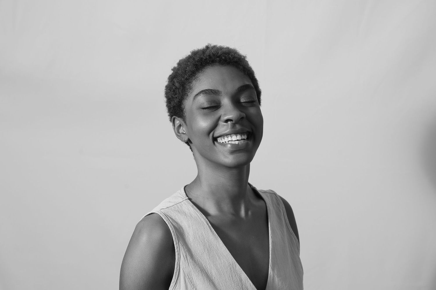 Black and white portrait of a smiling young woman with short hair wearing a sleeveless top against a light background.