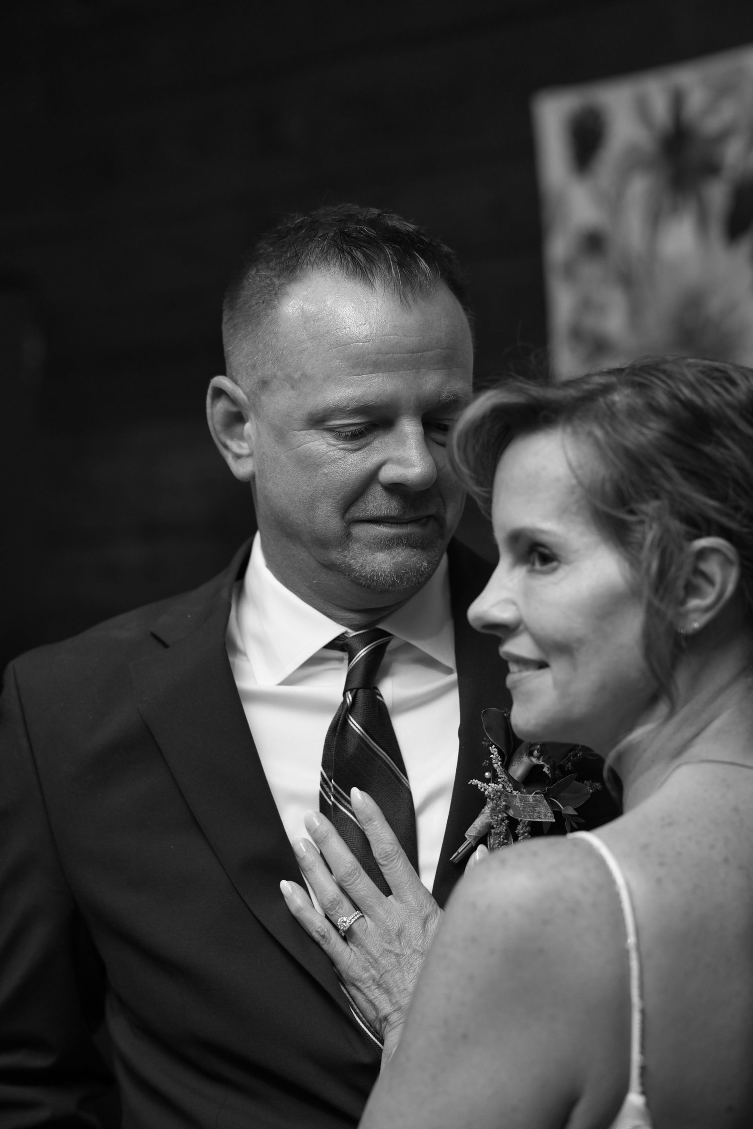 Black and white wedding photo of bride and groom sharing an intimate moment, bride's hand resting on groom's chest.