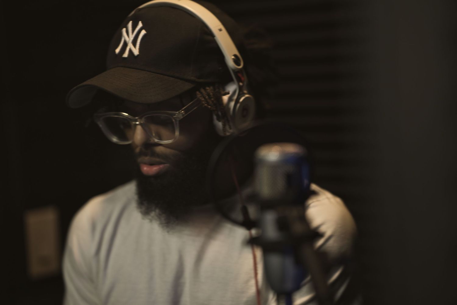 Man with NY cap and headphones recording in a professional music studio with a condenser microphone.