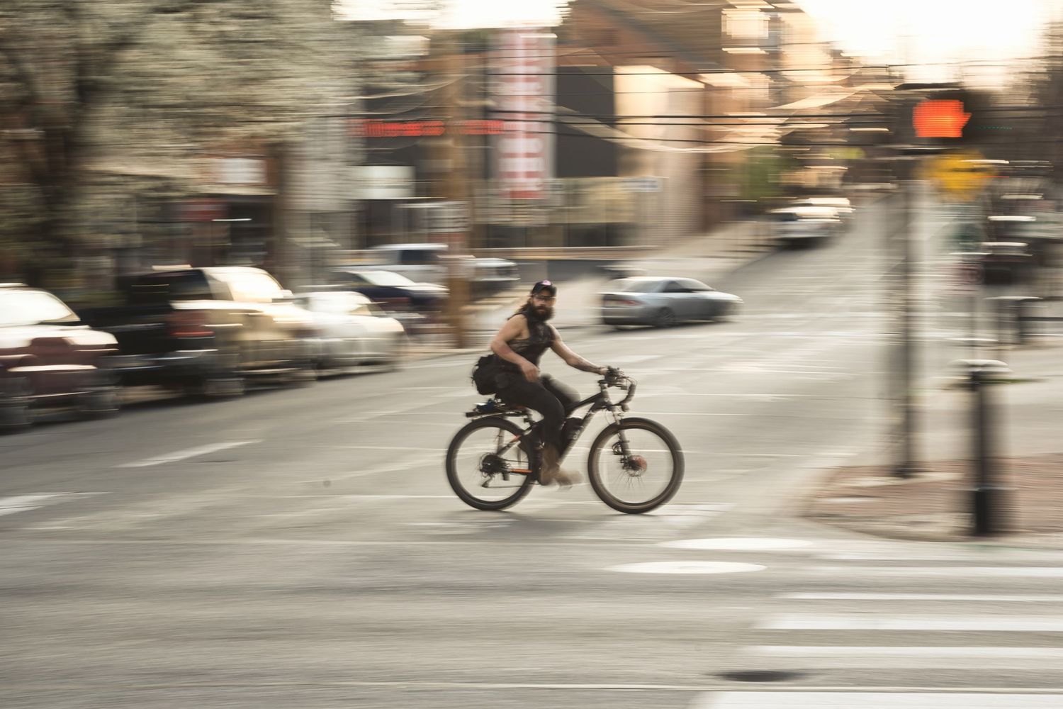 Cyclist riding through a busy urban intersection with motion blur, city streets and traffic lights visible in background.