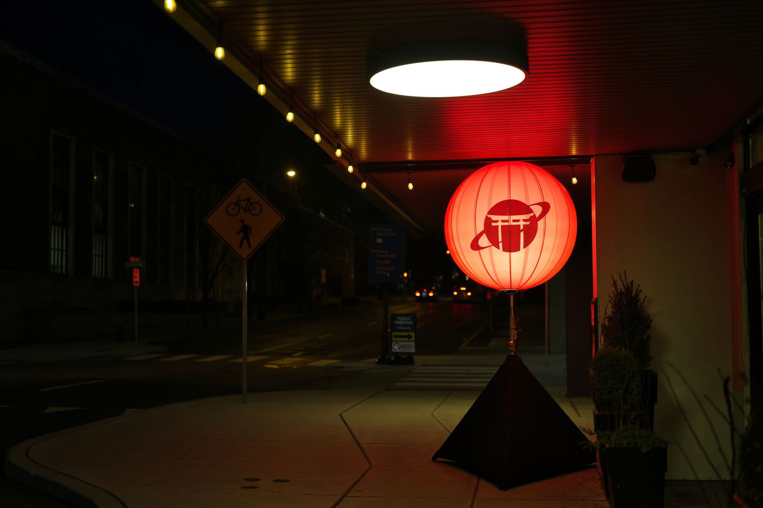 Red Japanese lantern glowing at night outside a restaurant entrance with string lights and a yield sign.