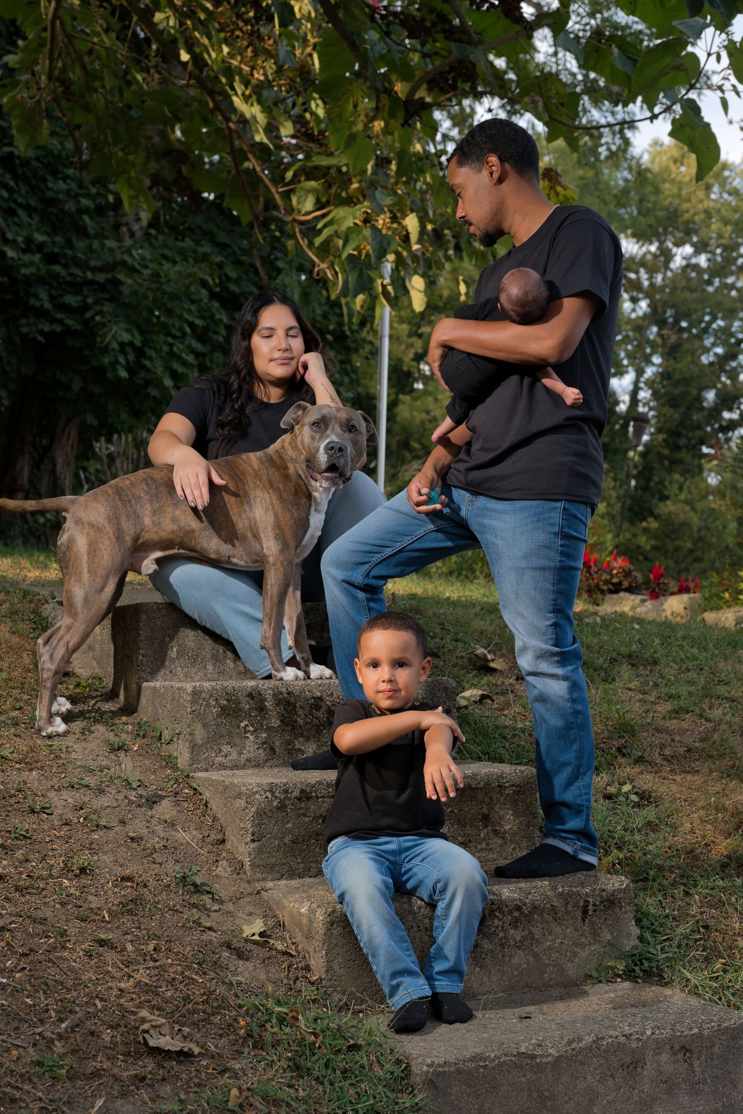 Family of four with a large brindle dog posing on stone steps in a park, wearing matching black shirts and jeans.