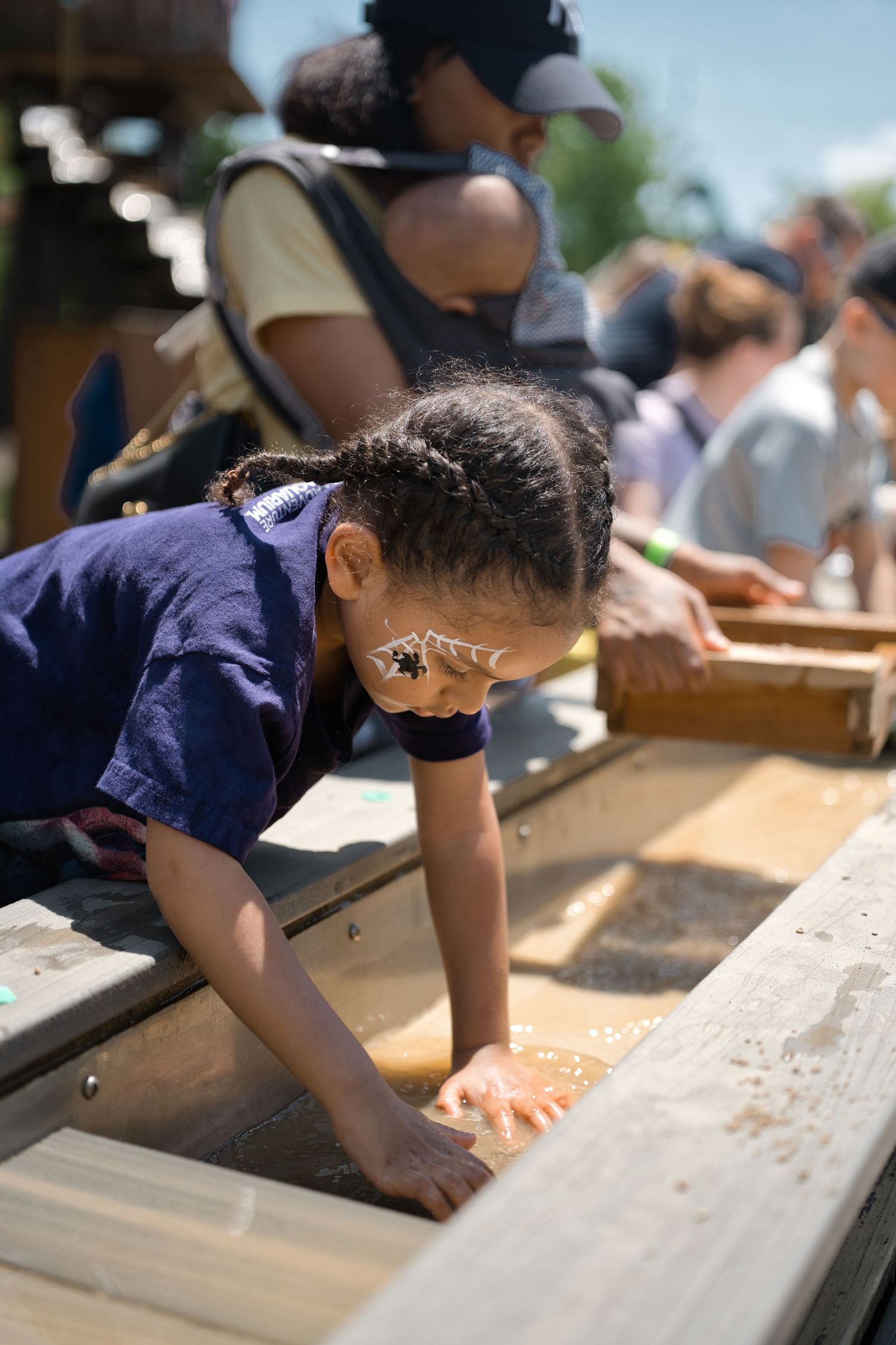 Child leaning over wooden planks during outdoor construction or building activity.