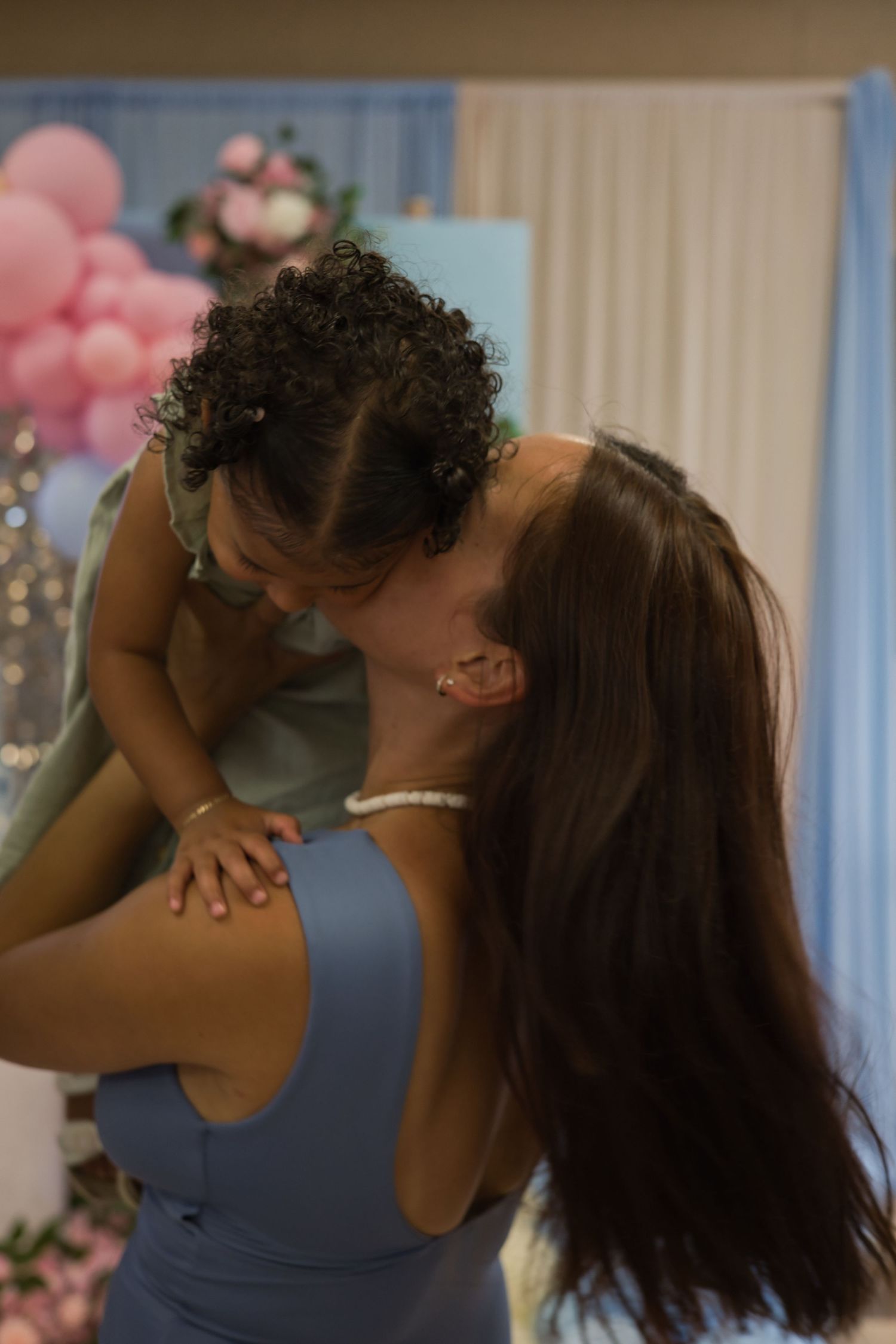 Tender moment captured at a party with pink balloons and blue decorations in background.
