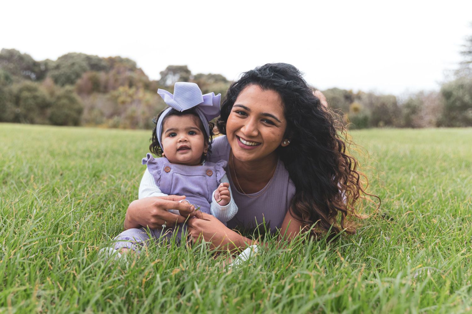 Auckland North Shore Mum and Baby Photos: Candid moment of mother and infant resting together in a grassy park field.