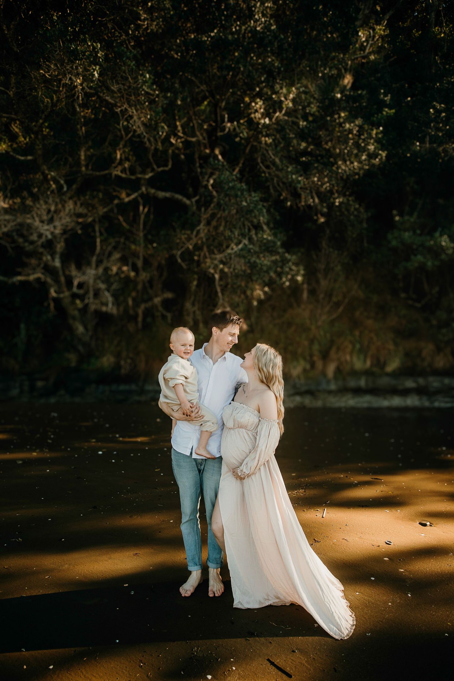 Auckland Maternity Photos: Pregnant woman and partner cudding at Long Bay Beach sunset for family photos.