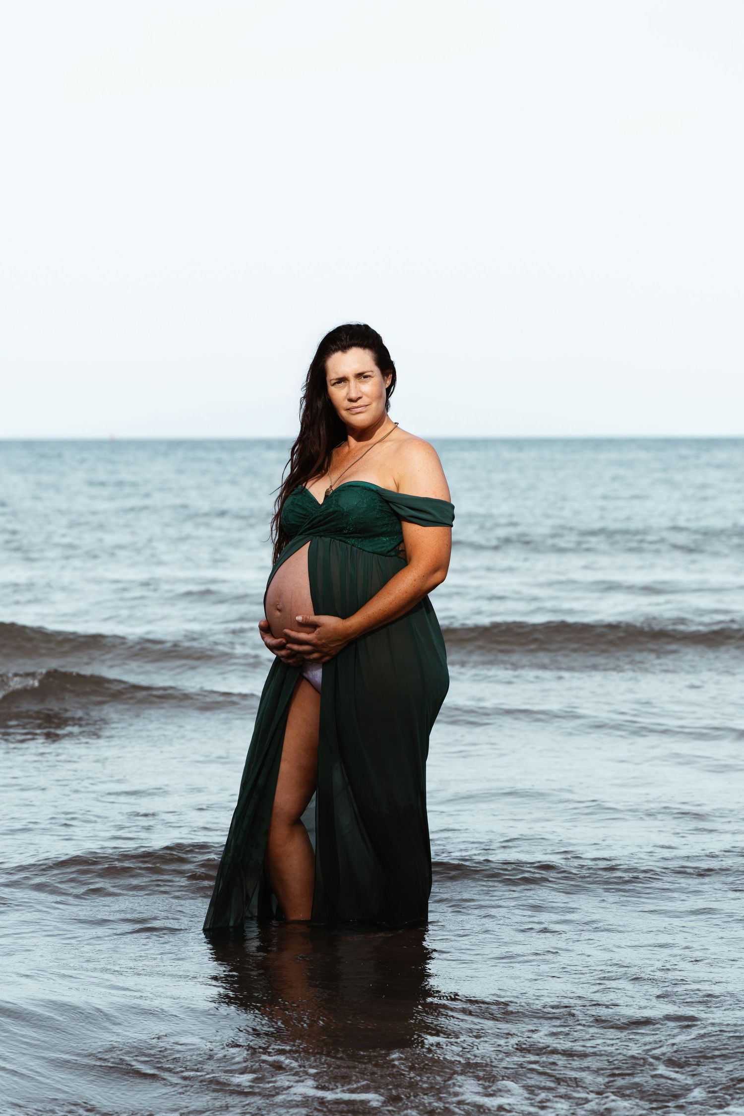 Pregnant woman standing in the sea at an Auckland beach during a natural maternity session by an Auckland photographer.