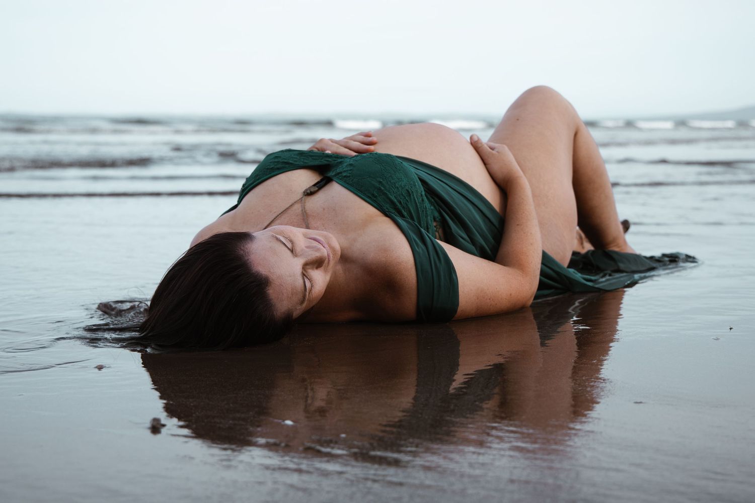 Pregnant woman laying in the sea at an Auckland beach during a natural maternity session by an Auckland photographer.