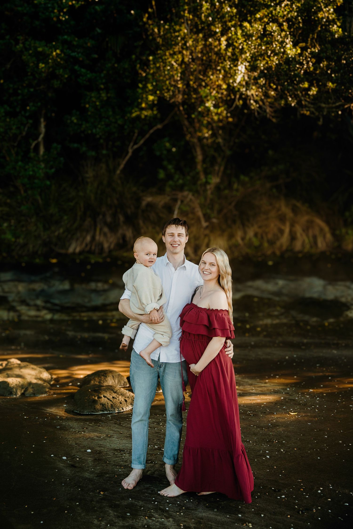 Auckland North Shore Family Maternity: Mum in red dress, dad, and son posing on the beach at sunset.