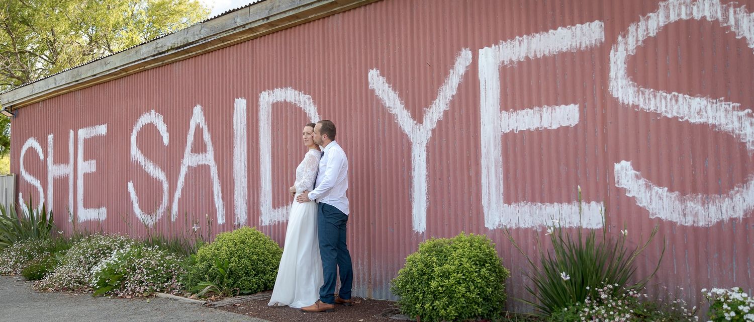 Auckland North Shore Wedding: Couple smiling in front of the 'She Said Yes' barn wedding venue  photographed by Shara-Lee.