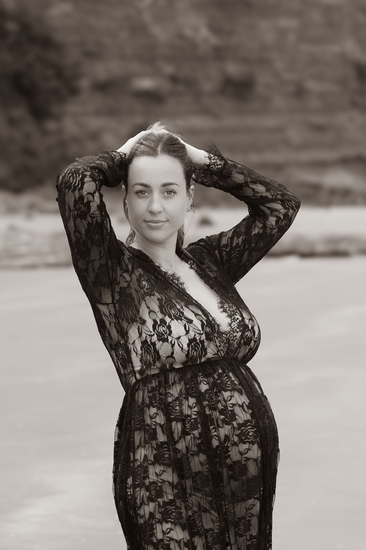 Auckland North Shore Maternity Portrait: Pregnant woman in black lace dress posing dramatically on the beach.