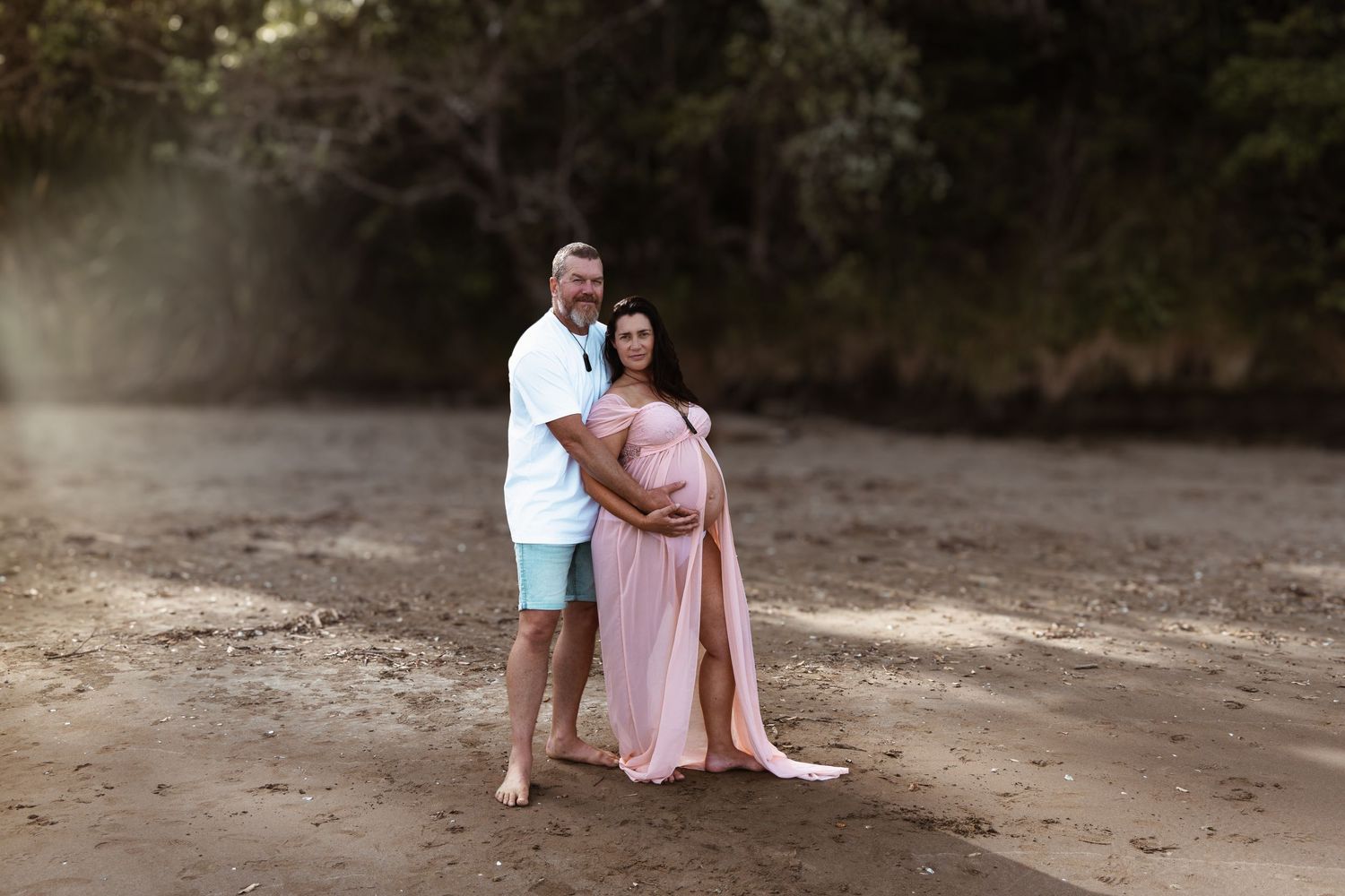 Expectant couple standing together on a sandy Auckland beach during a maternity session by an Auckland photographer