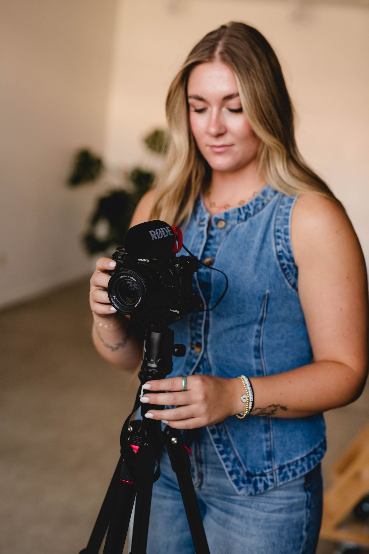 Emilie in denim outfit adjusts camera settings on tripod while working in indoor studio setting.