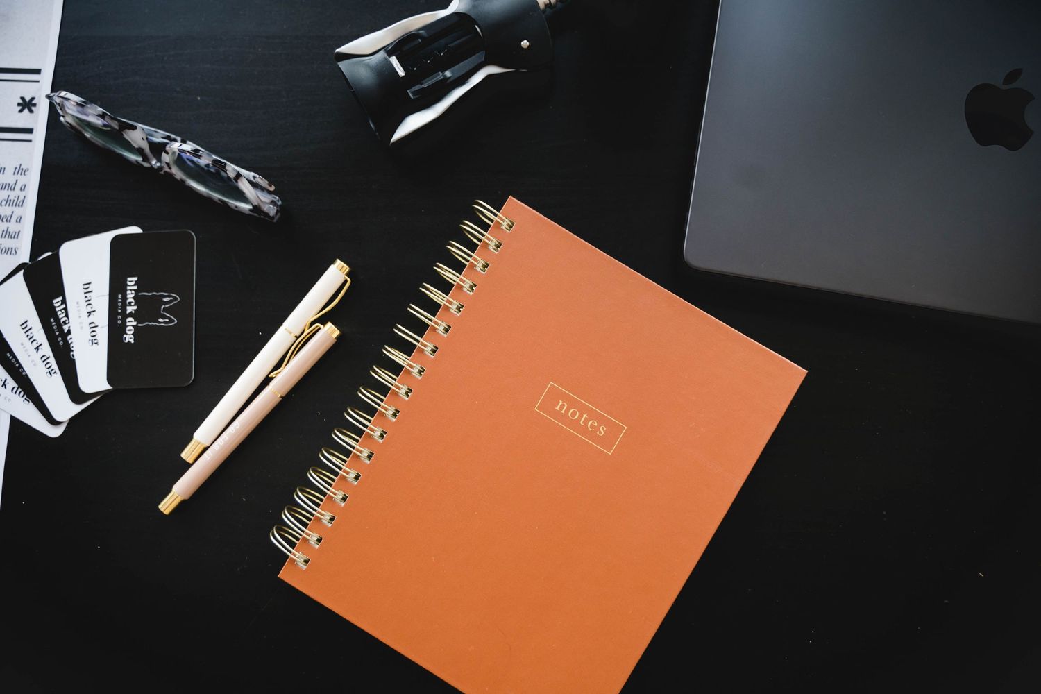 Dark minimalist flatlay with notebook, pencils and office supplies.