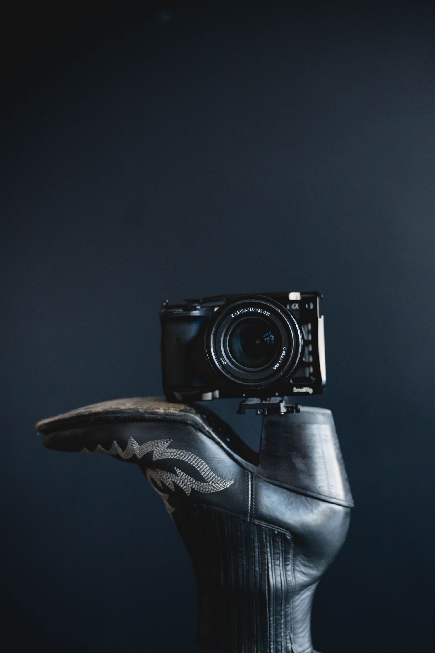 Professional camera mounted on leather boot in dramatic dark lighting.