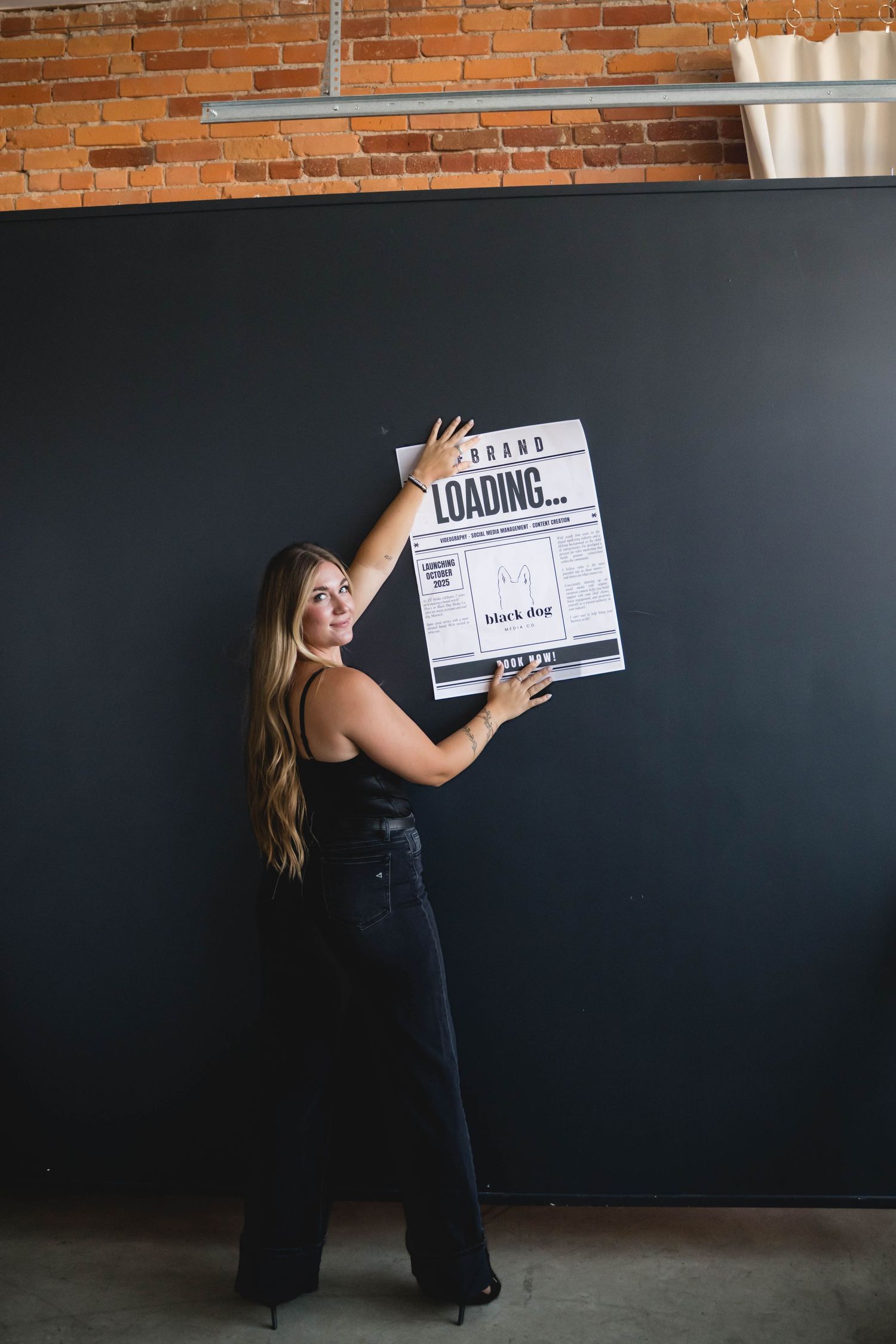Woman in black outfit holding loading sign against brick wall for creative photoshoot.