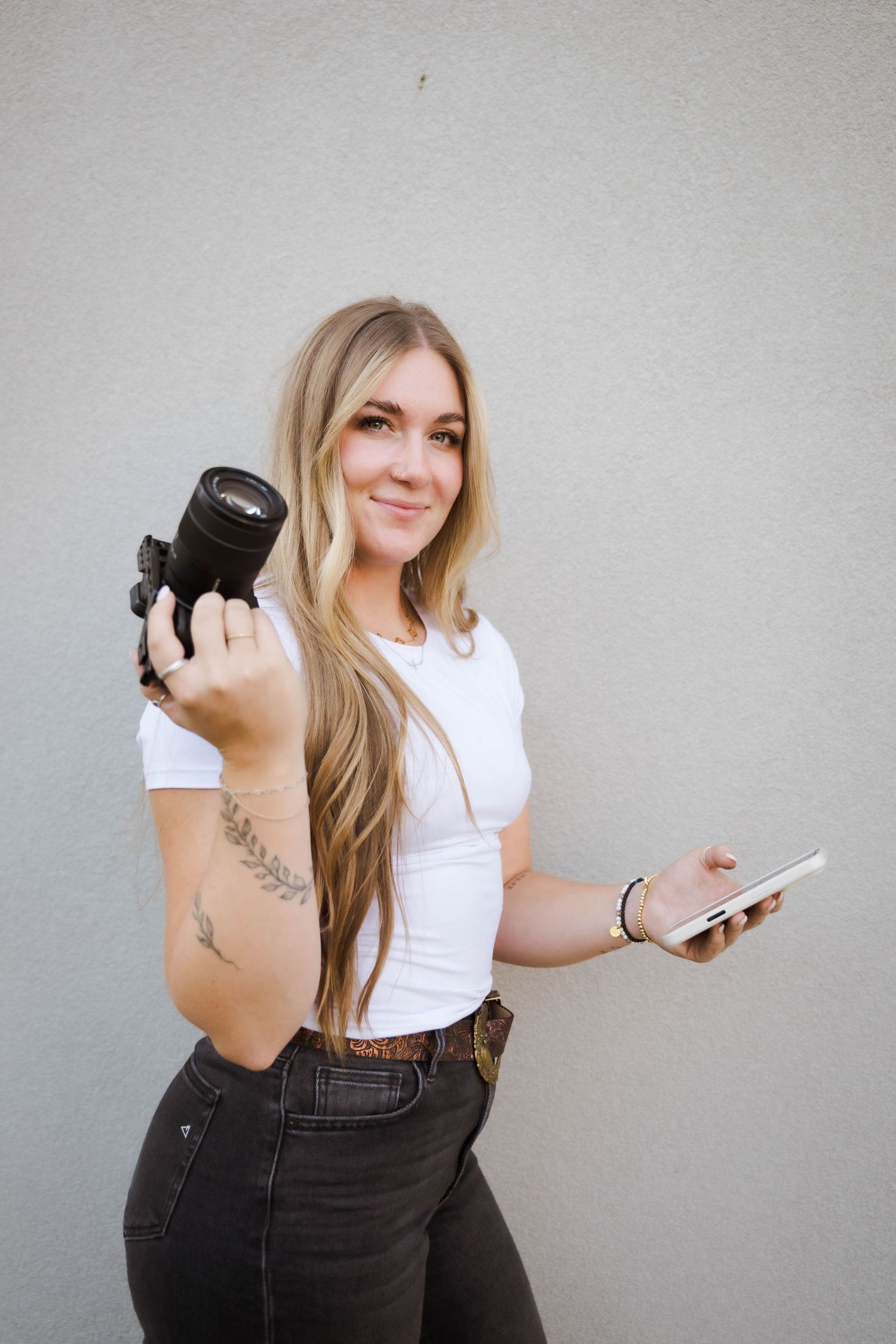 Emilie photographer holding camera equipment against grey wall.