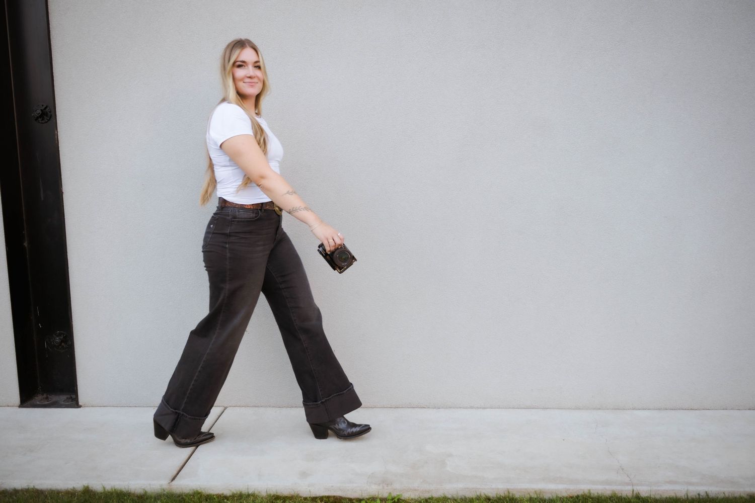 Emilie in black pants and white top performs a dynamic dance move against a plain white wall.