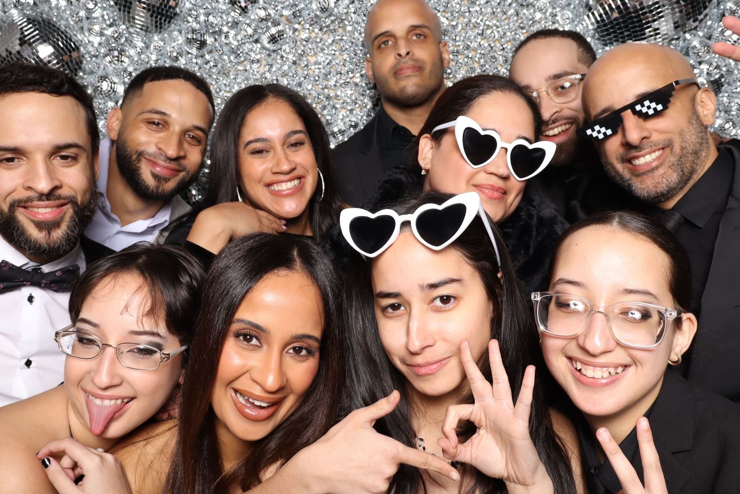 Large group in formal attire poses together against sparkly silver photo booth background.