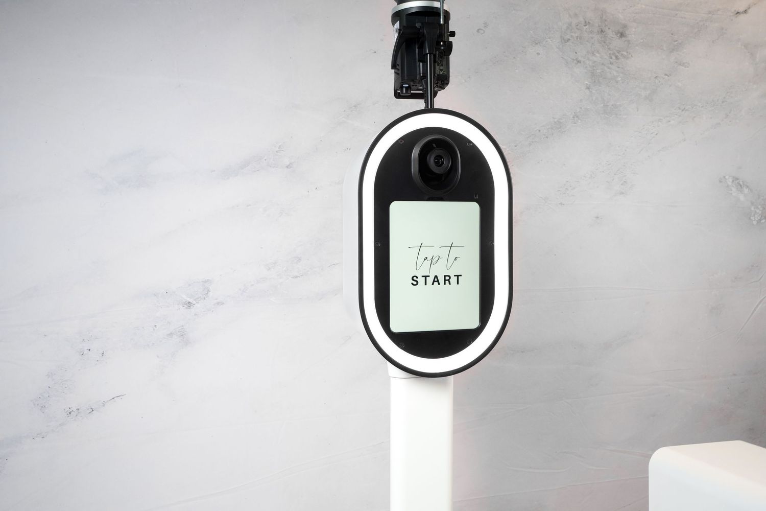 Sleek white photo booth kiosk with circular display mounted against marble wall.