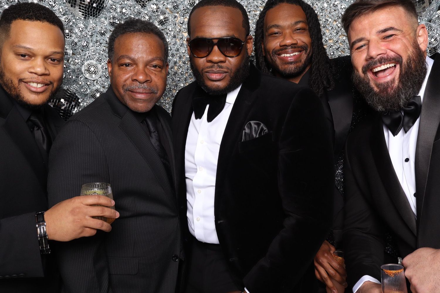 A group of men in formal black and white attire posing together and laughing at a social event.