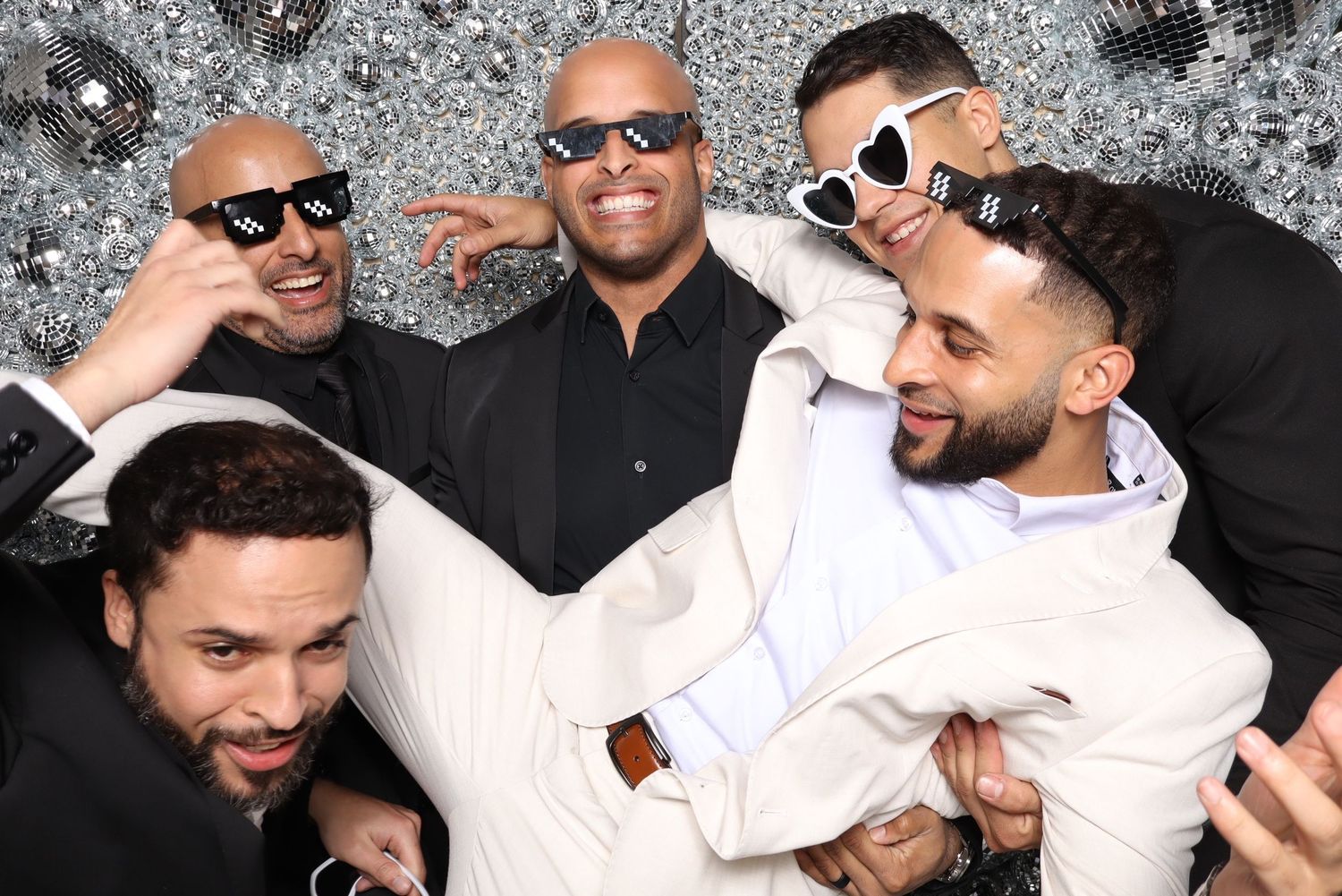 Men in formal attire and sunglasses smiling together at a photo shoot.