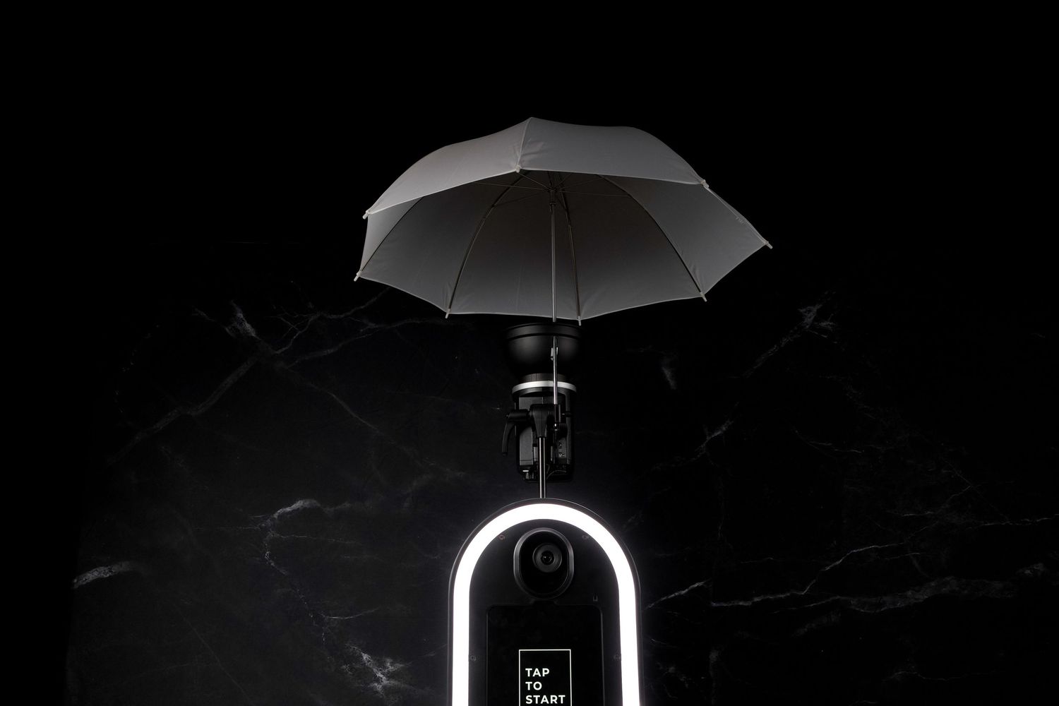 Black umbrella silhouetted against dark background with electronic device underneath.