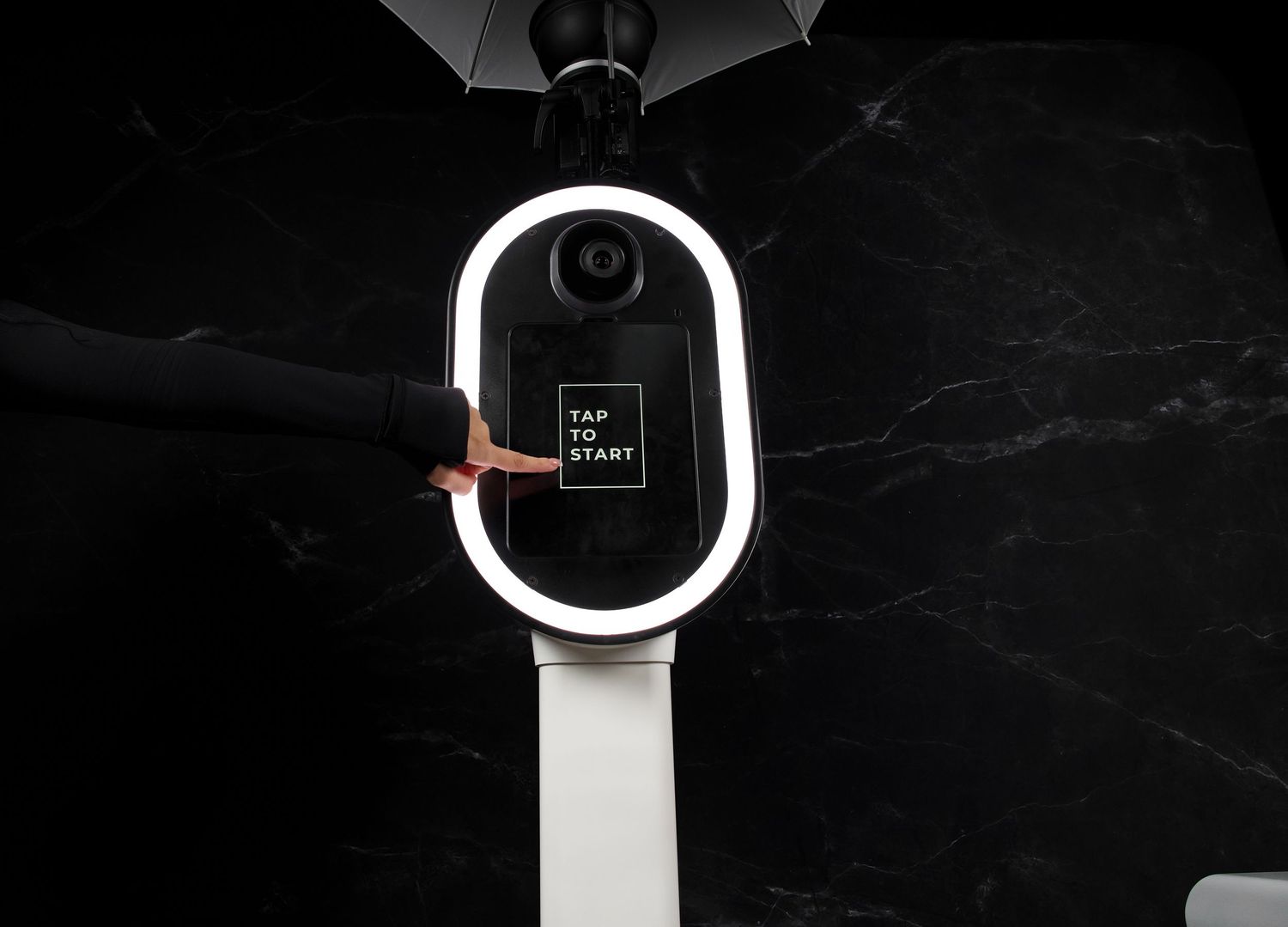 Modern photo booth kiosk with illuminated circular display shown in dramatic lighting.