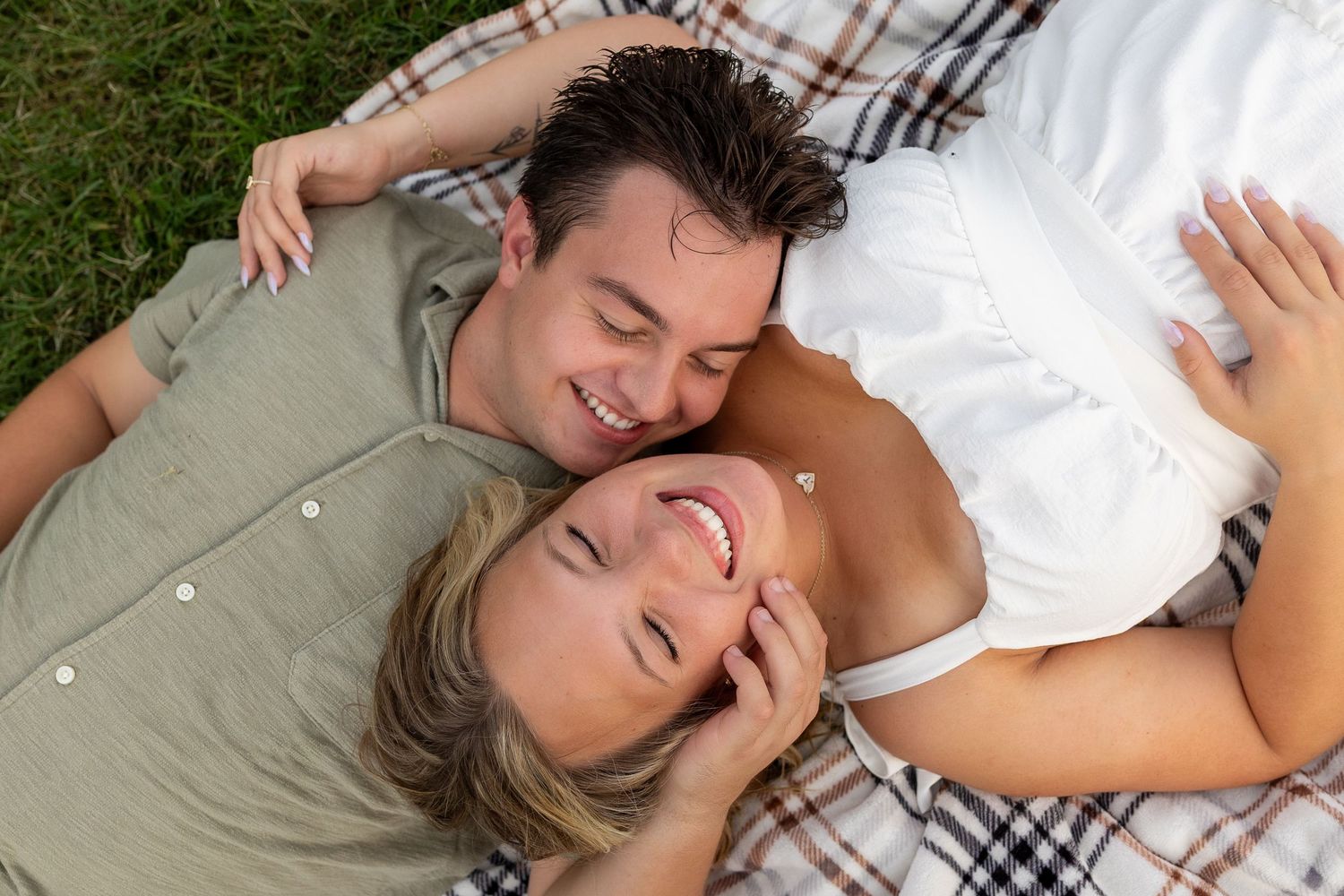 Happy couple lying on a plaid blanket in the grass, smiling and enjoying a romantic outdoor picnic together.