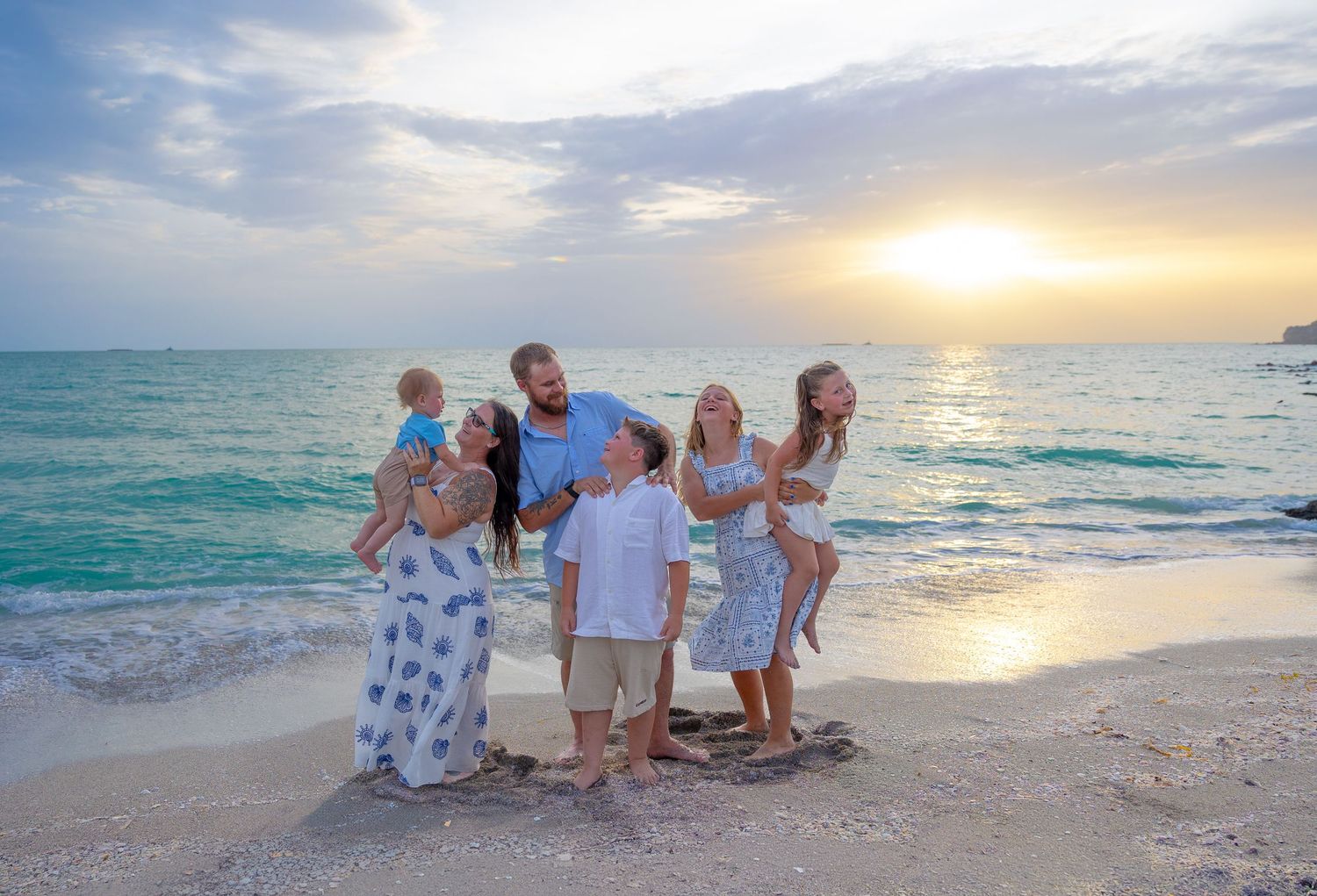 Family posing together on a sandy beach at sunset with turquoise ocean waves in the background.