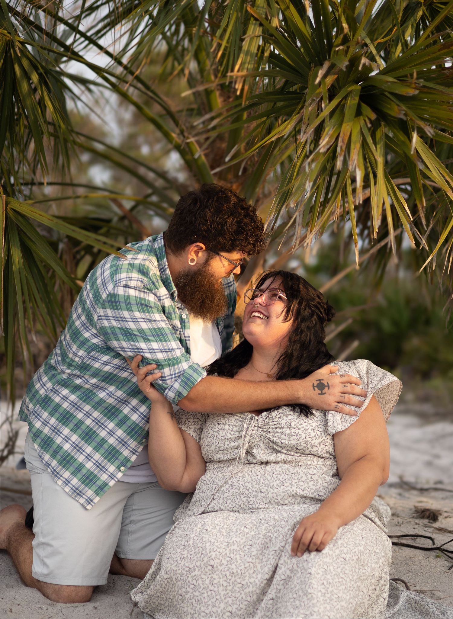 Couple sharing a romantic moment under palm trees on a sandy beach at golden hour.