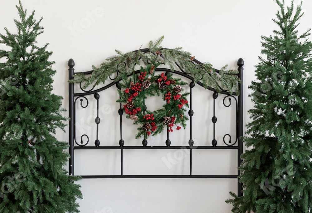 Black iron headboard decorated with a red berry wreath and green garland, flanked by two Christmas trees on white background.