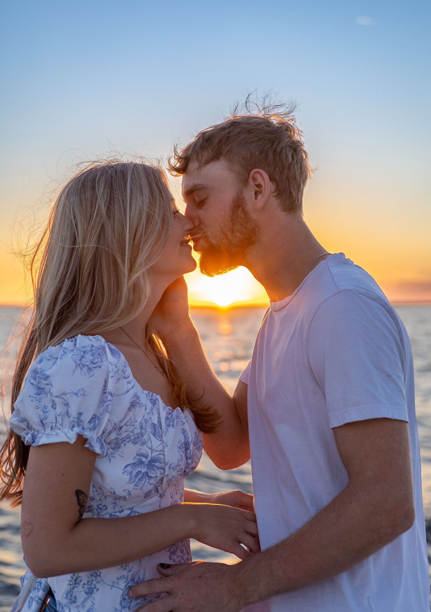 Couple shares a passionate kiss silhouetted against a vibrant orange and blue beach sunset.