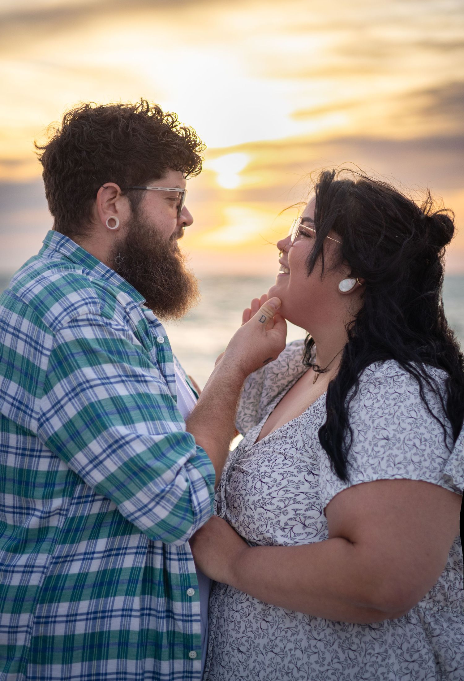 Romantic couple gazing at each other during a stunning beach sunset, man tenderly holding womans chin.
