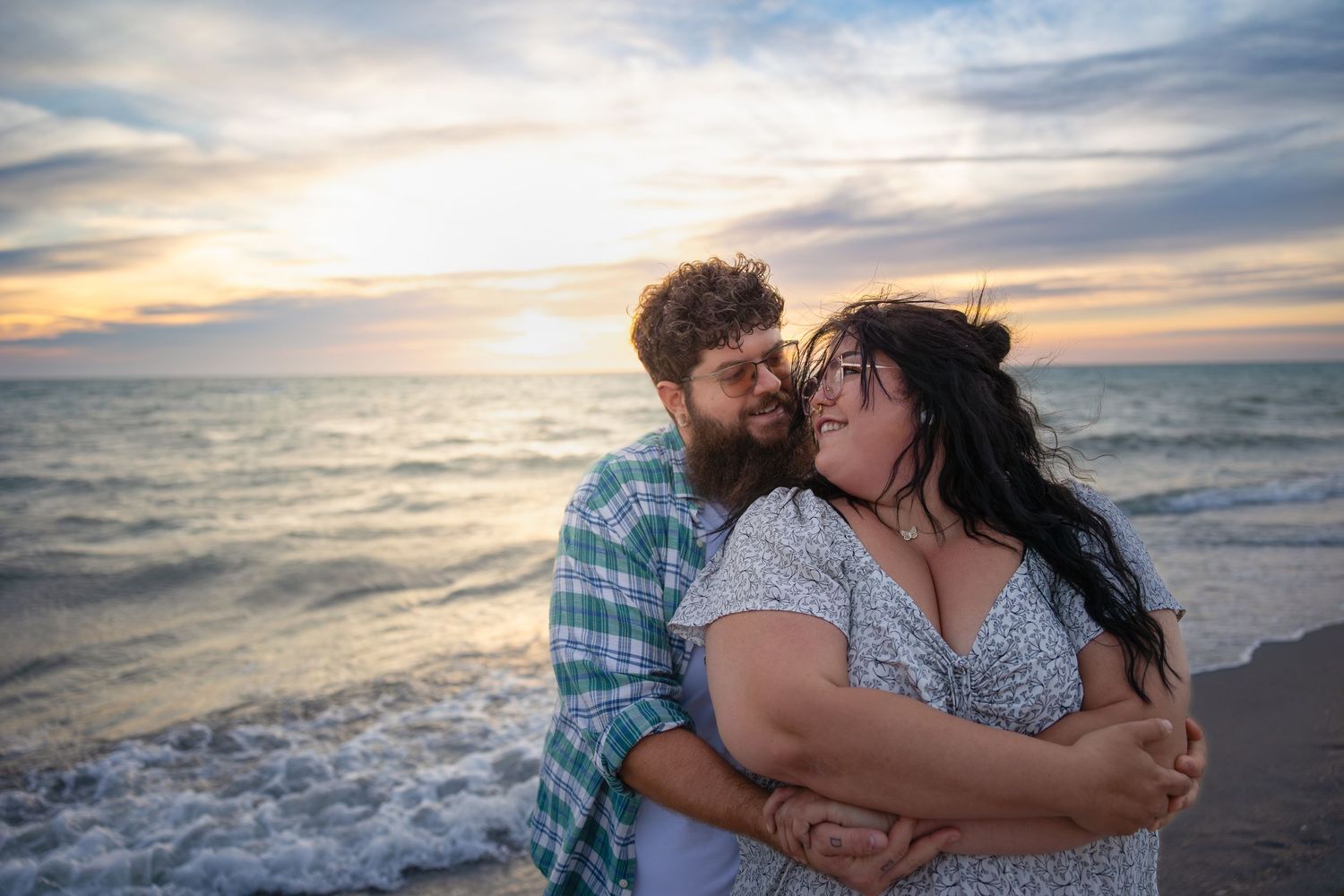 Loving couple embracing on a beach at sunset, man kissing womans cheek near ocean waves.