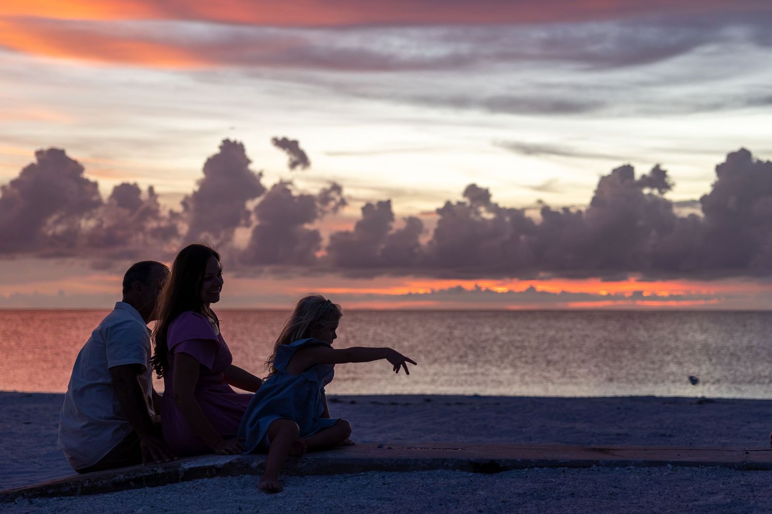 Silhouette of a family sitting on a beach watching a vibrant pink and purple sunset over the ocean.