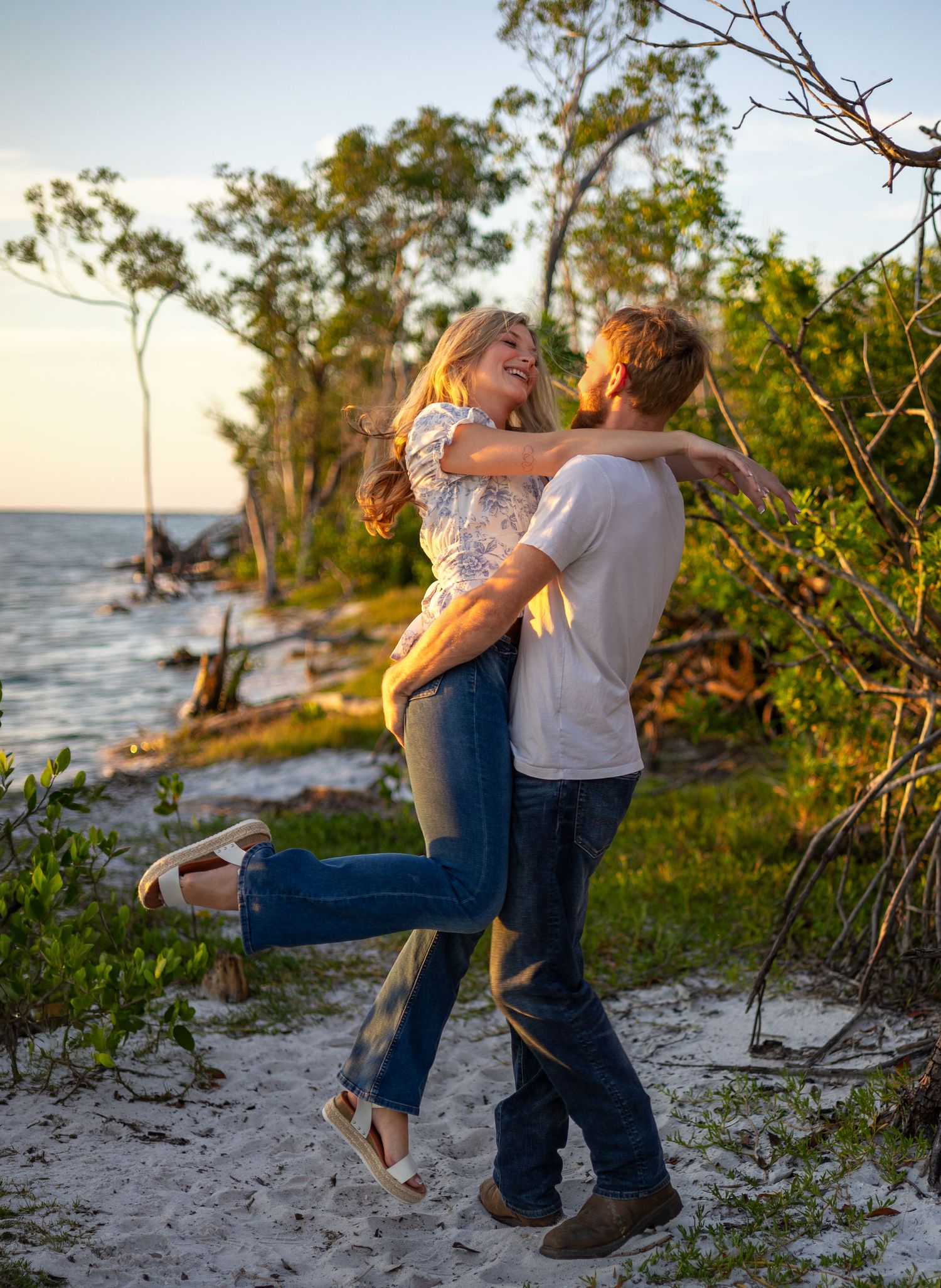 Happy couple spinning together on a sandy beach at golden hour with ocean views behind them.