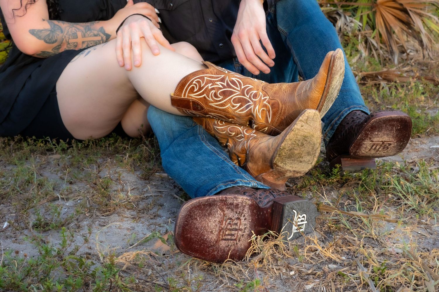 Two people sitting outdoors wearing decorative Western cowboy boots, showcasing intricate leather tooling designs.