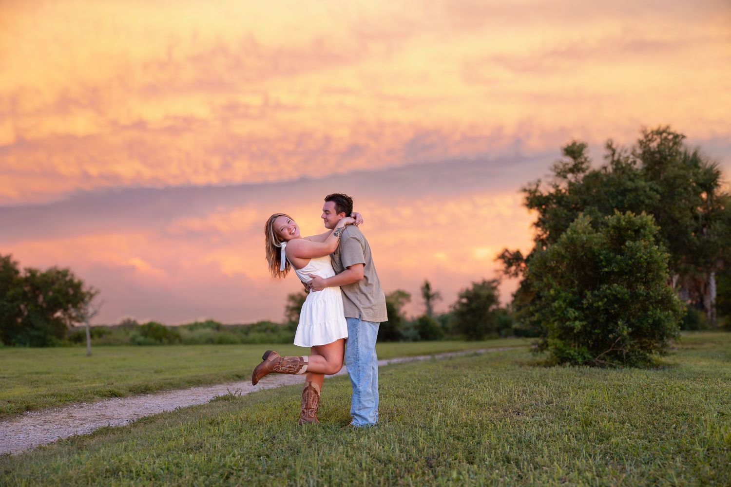 Romantic couple embracing and dancing in field during vibrant pink and orange sunset.