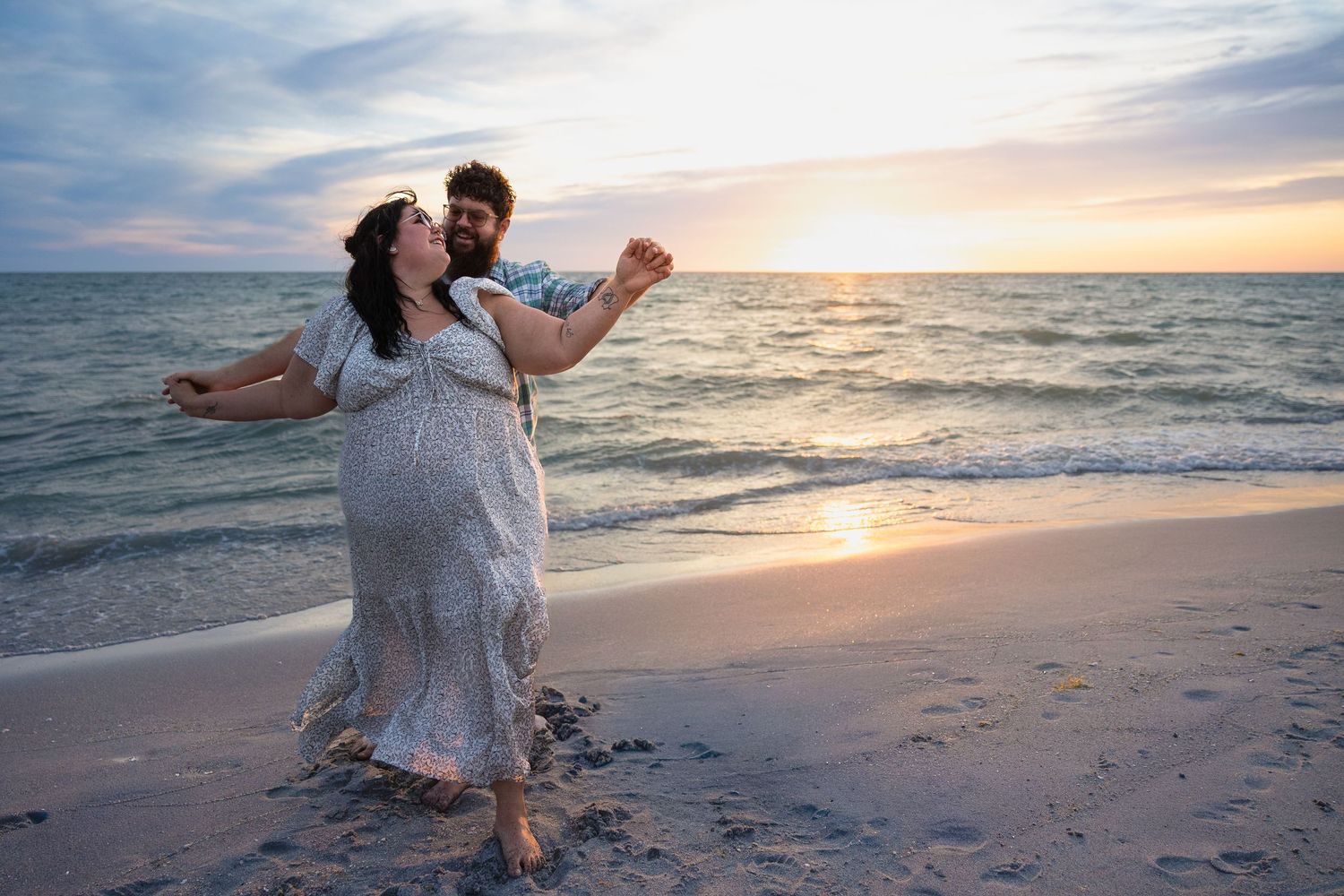 Happy couple spinning and dancing on a beach during a vibrant colorful sunset by the sea.