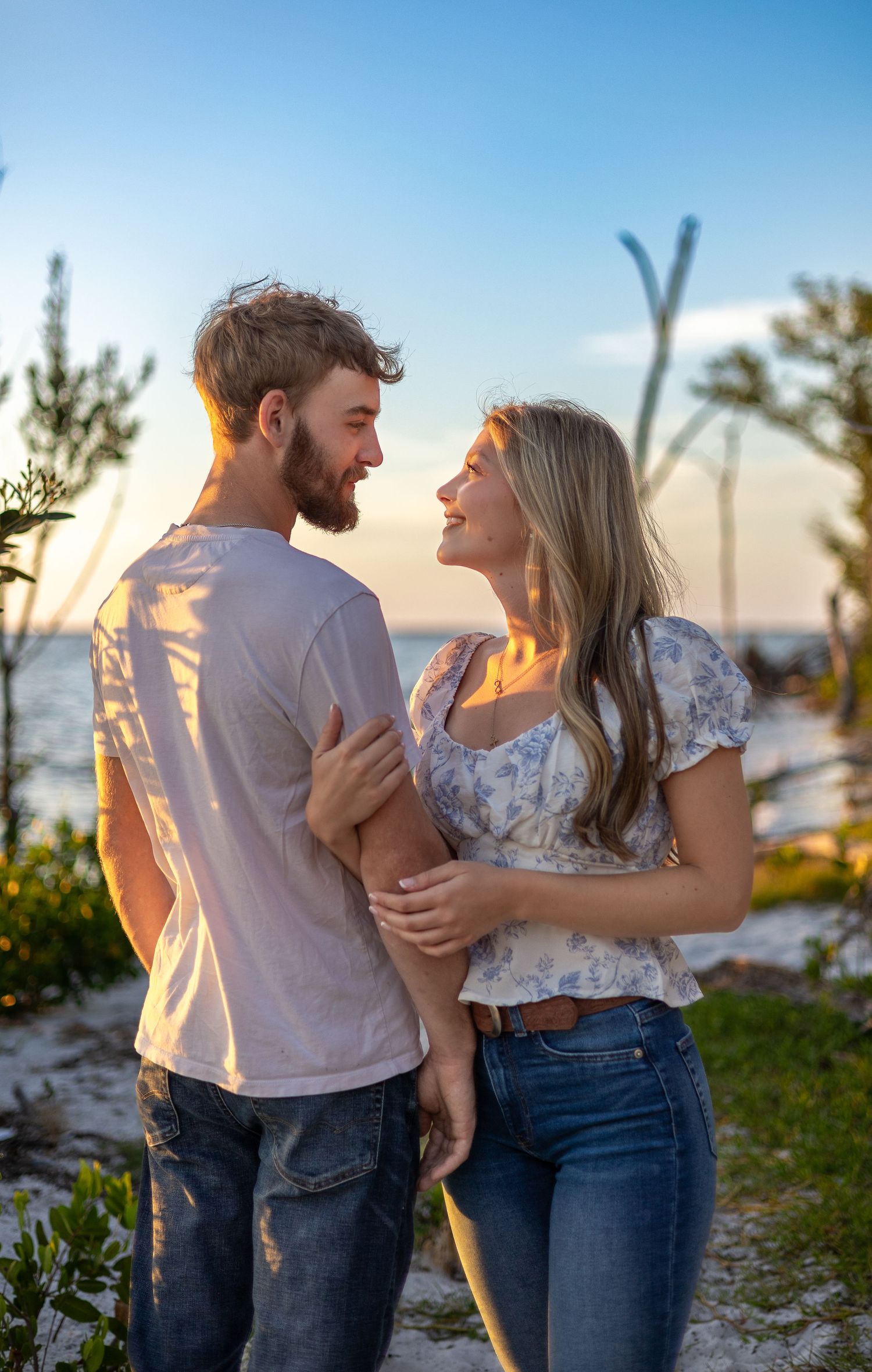 Smiling couple gazes lovingly at each other during a romantic beach sunset photoshoot.
