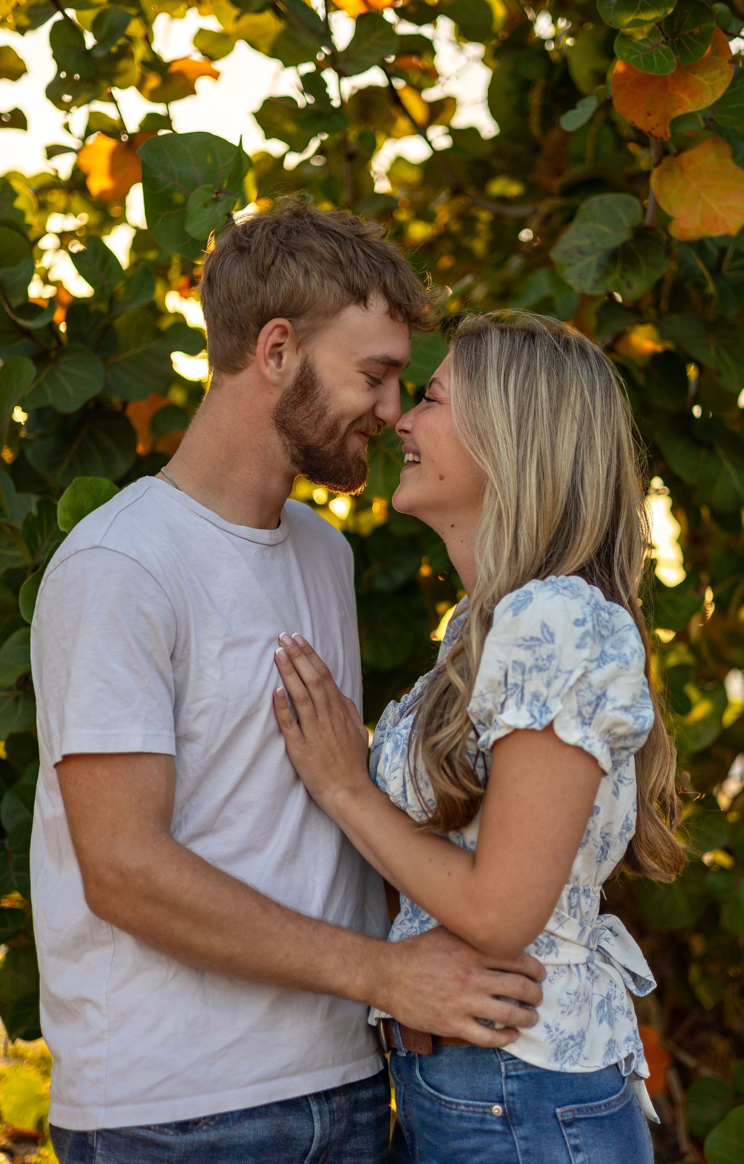 Romantic couple nearly kissing while embracing in front of a colorful fruit tree at golden hour.