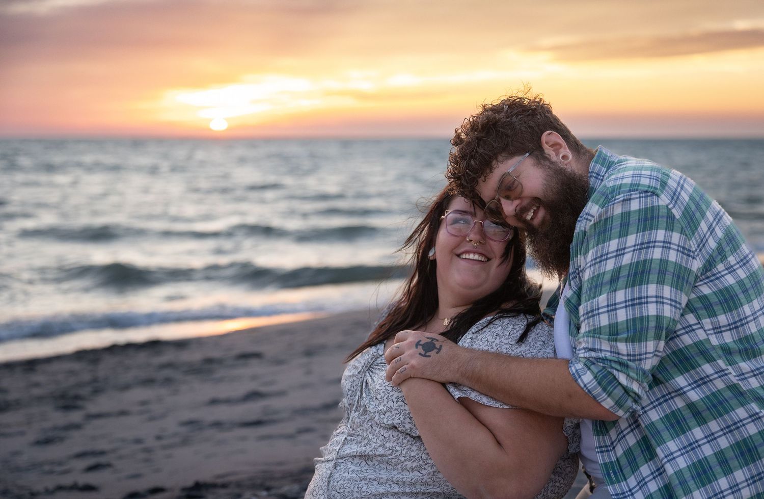 A happy couple embracing and laughing together on a beach during a golden sunset.
