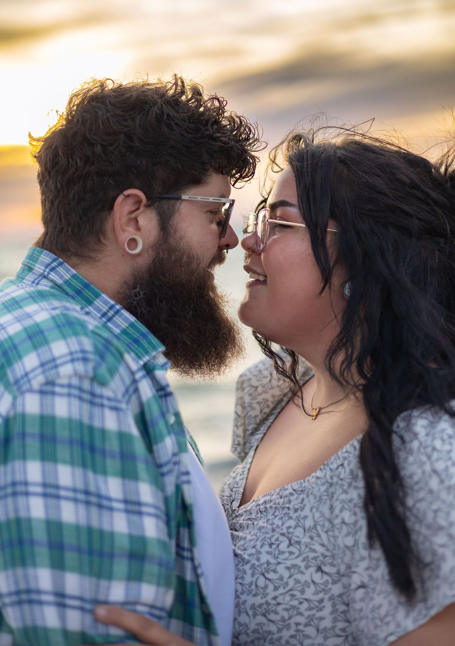 Romantic couple nearly kissing at sunset on a beach, man with curly hair and beard, woman with long dark hair.