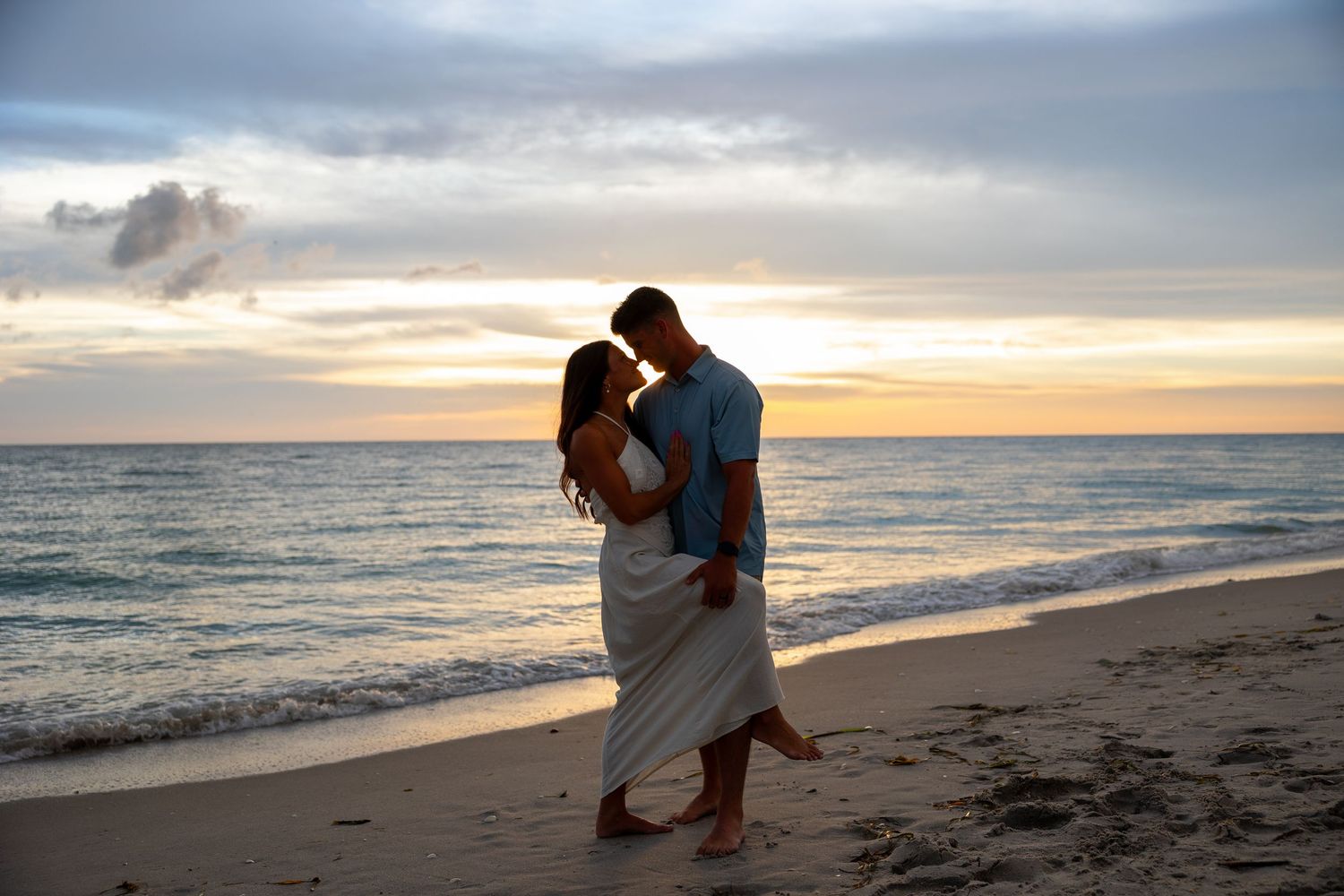Romantic couple embracing on a tropical beach at sunset with golden skies and ocean waves.