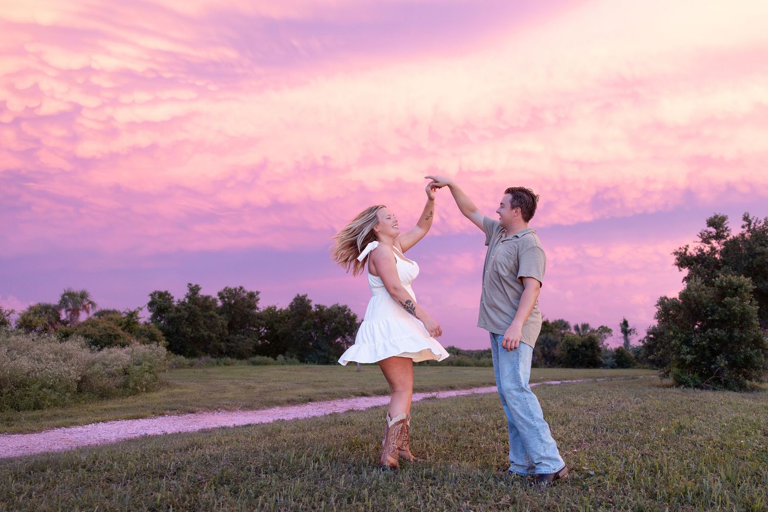 Couple dancing together in a field at sunset with a stunning pink and purple sky backdrop.