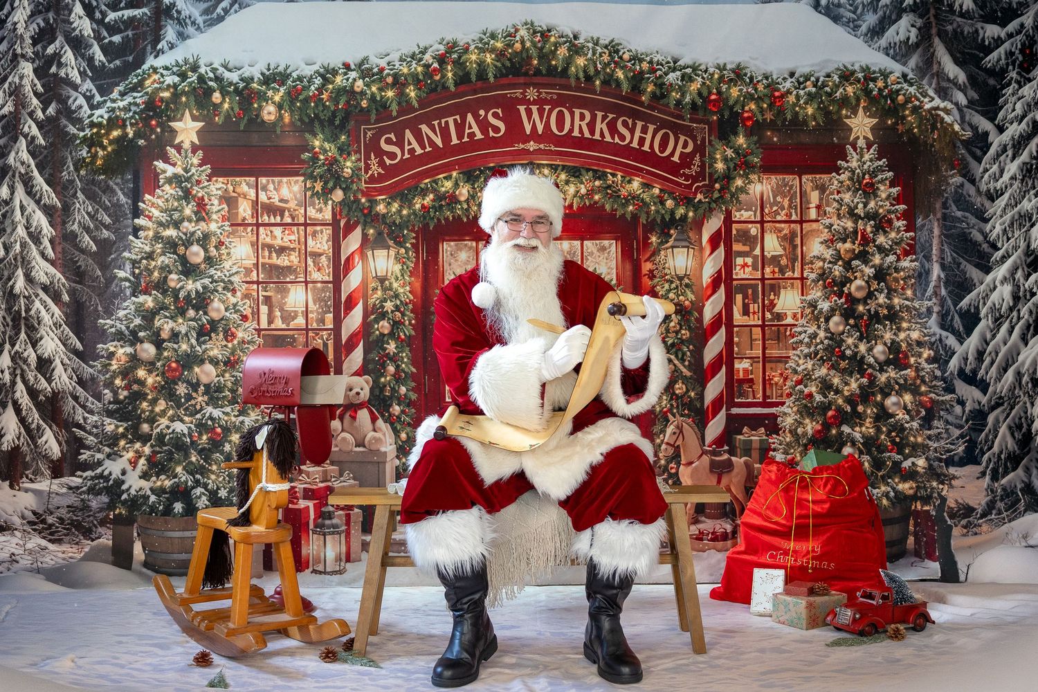 Santa Claus sits in a chair at his workshop, holding a scroll, surrounded by Christmas trees and holiday decorations.