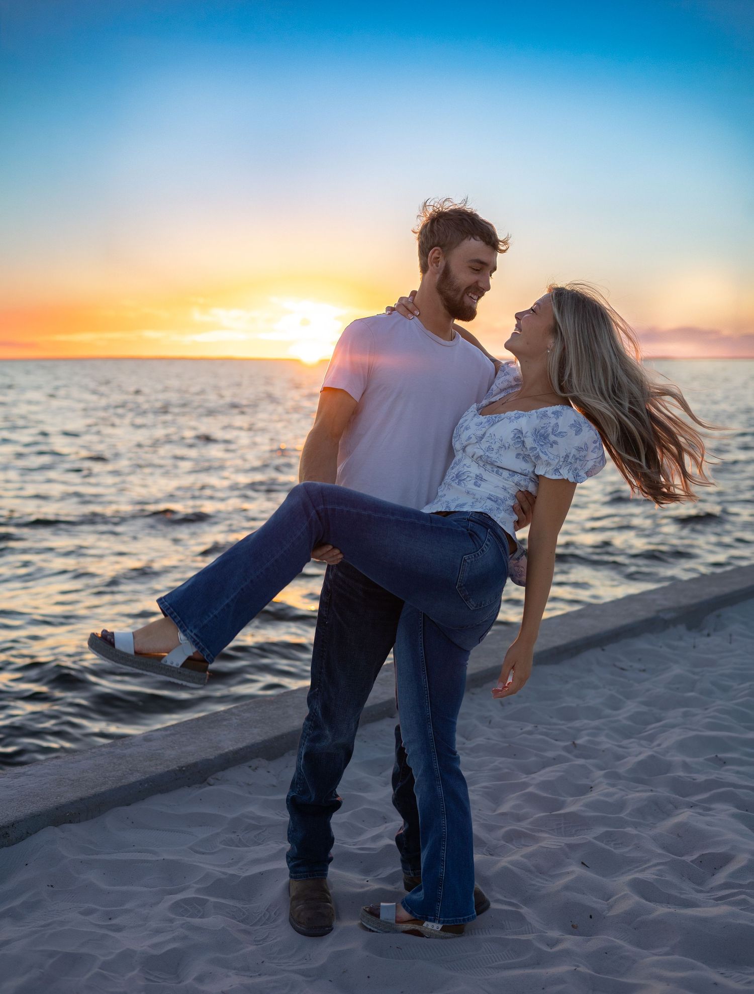 Man lifting woman in his arms on sandy beach at golden sunset.