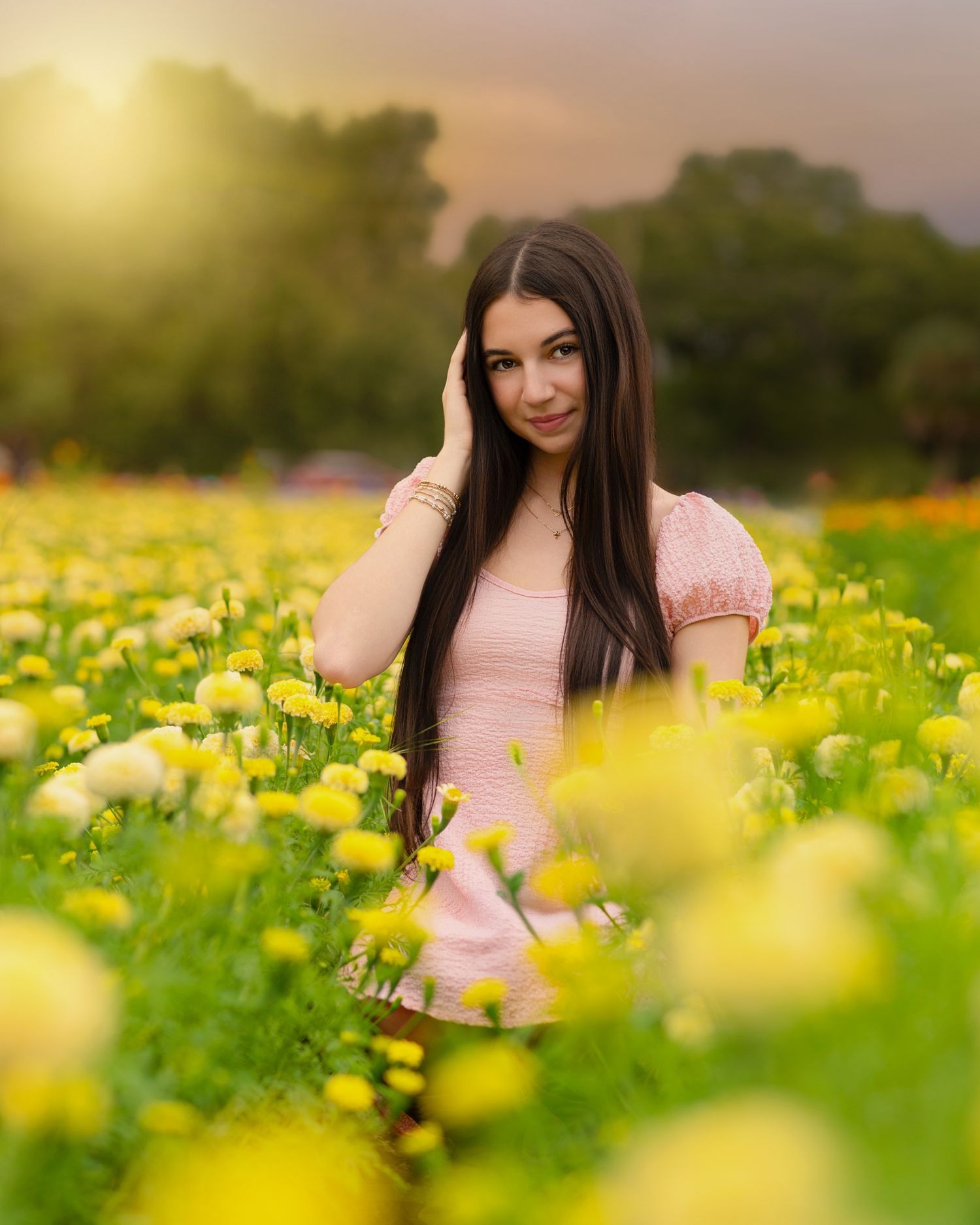 Young woman with long dark hair in pink dress posing in a field of yellow flowers.